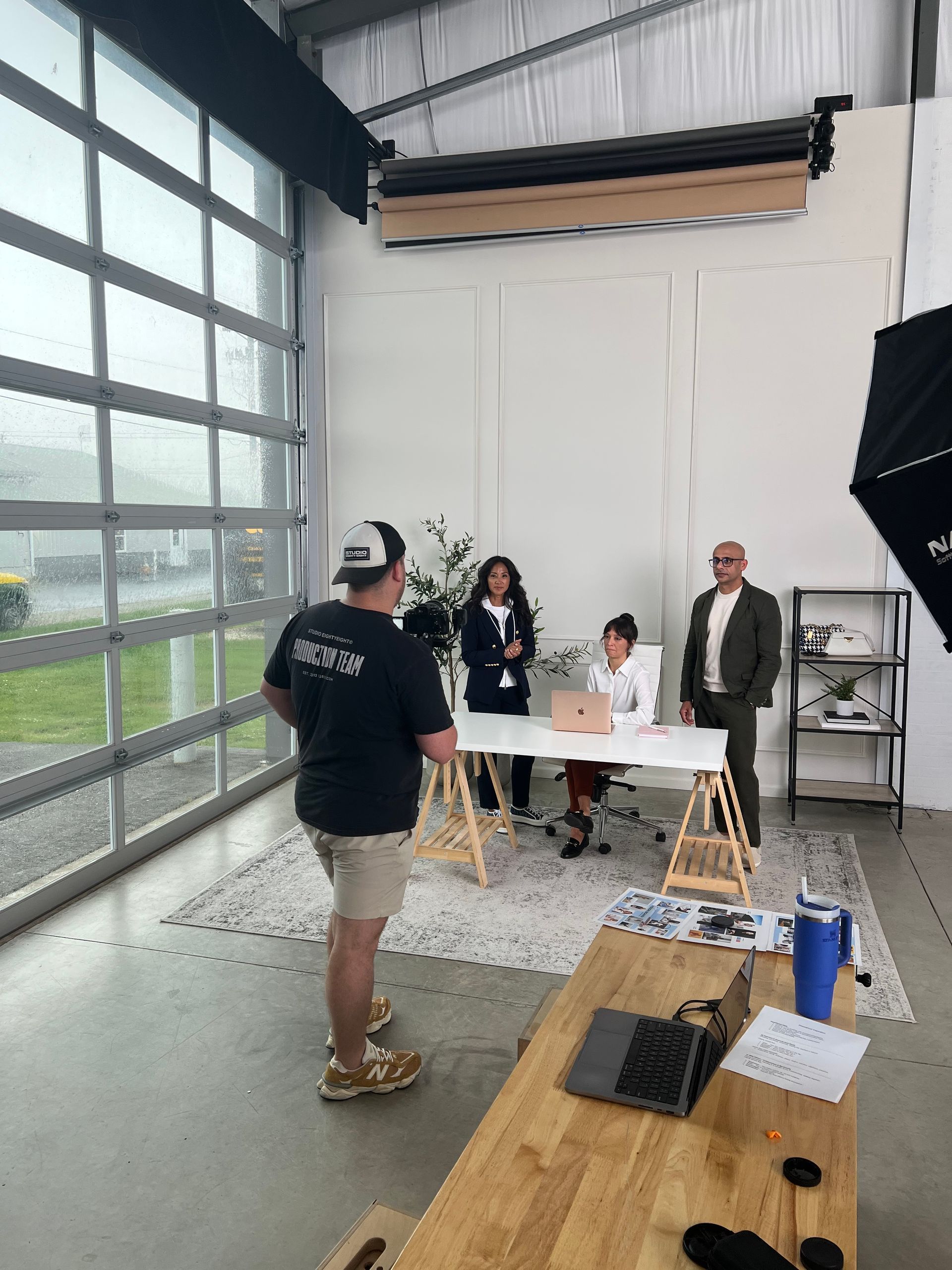 Video shoot in a studio: crew member, three people at a white table, backdrop, equipment.